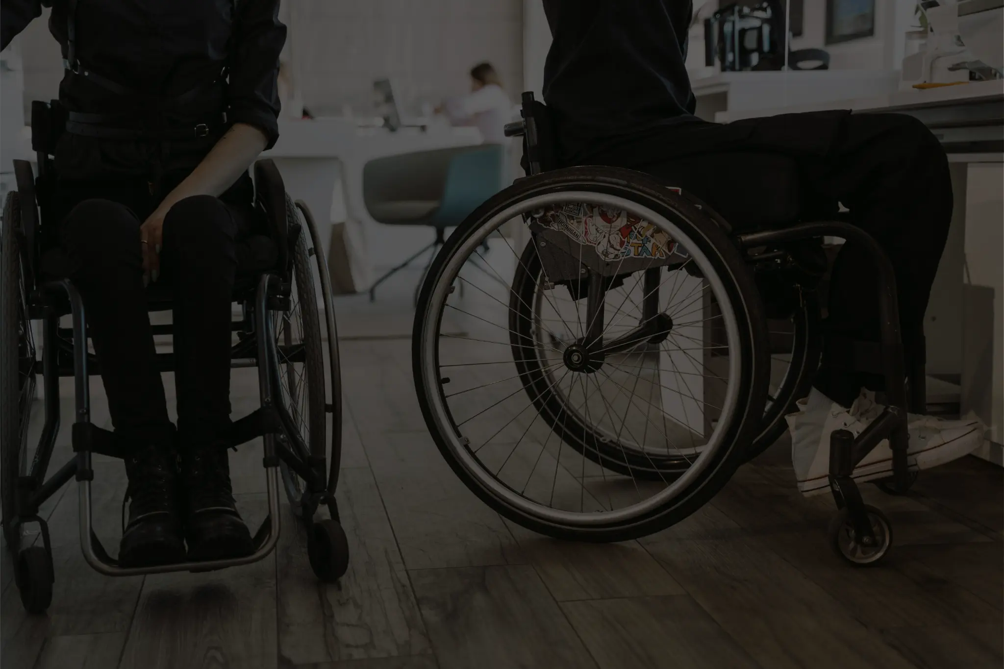 Two people in wheelchairs at workspace.